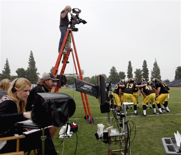 Tecia Esposito, left, watches a computer monitor during the filming of a television commercial at Birmingham High School football field in Los Angeles. 